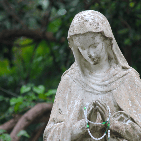 weathered statue of Mary with green Rosary on her hands