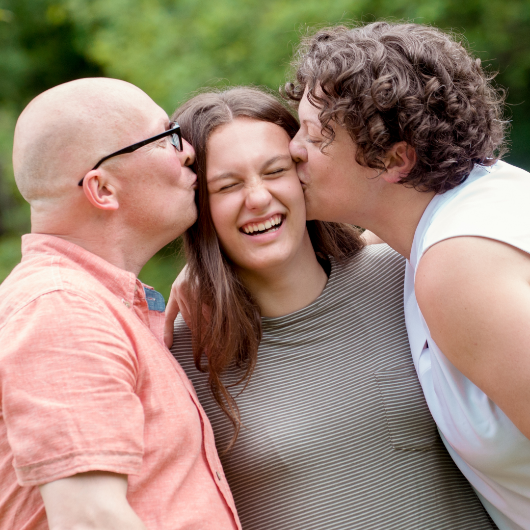 teenager laughing while mom and dad give her a kiss