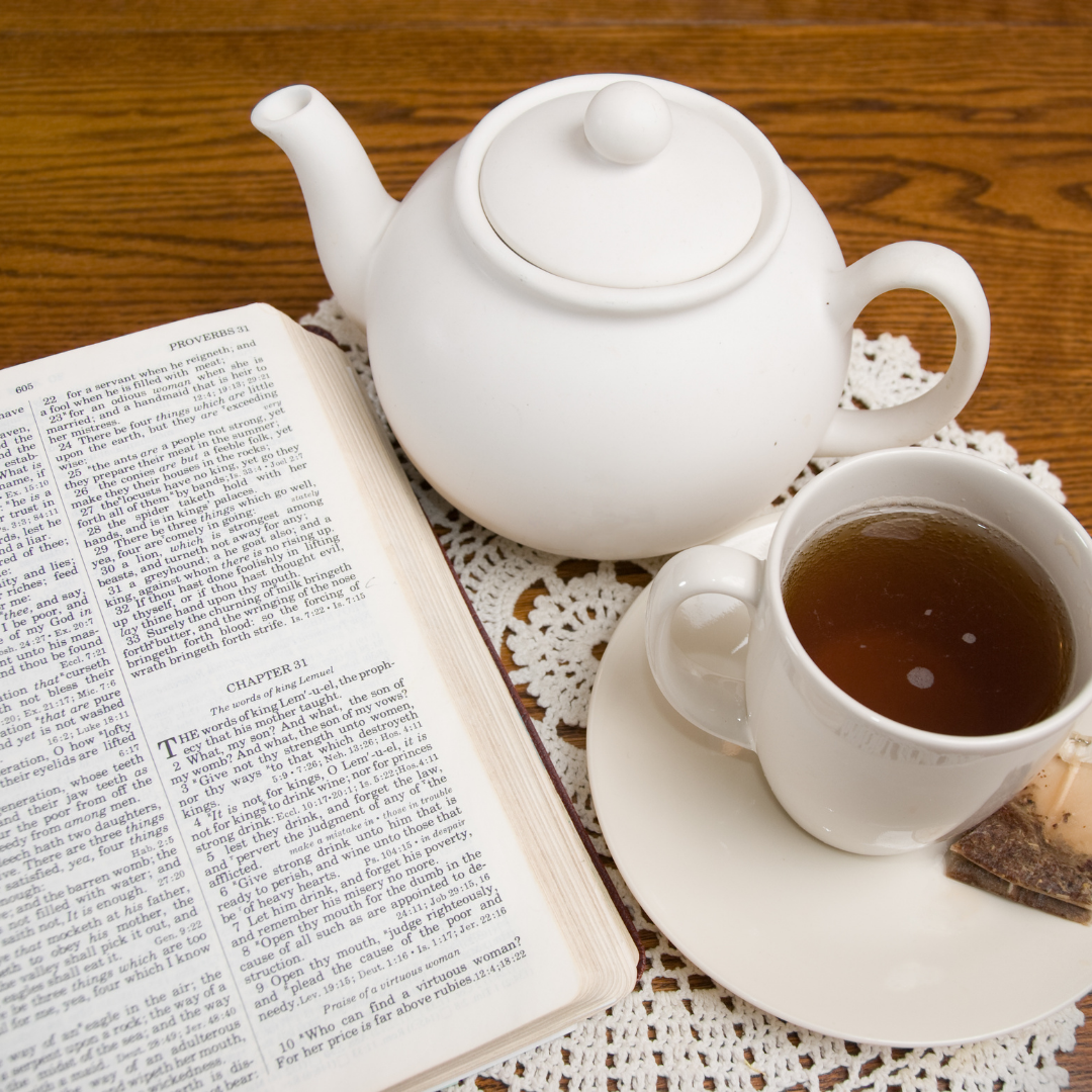 Open bible next to white teapot and teacup