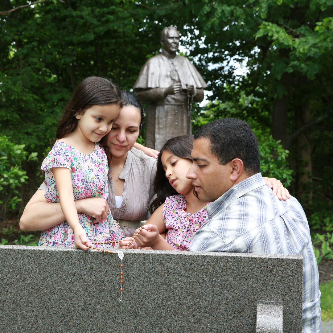family praying the Rosary near a statue of Fr. Patrick Peyton