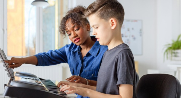 trainer-showing-sheet-to-student-and-playing-piano-picture-id1149780540